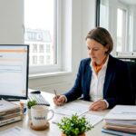 Eine Hausverwalterin sichtet und bearbeitet WEG-Unterlagen an ihrem Schreibtisch.