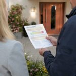 Hände halten Energieausweis am Hauseingang